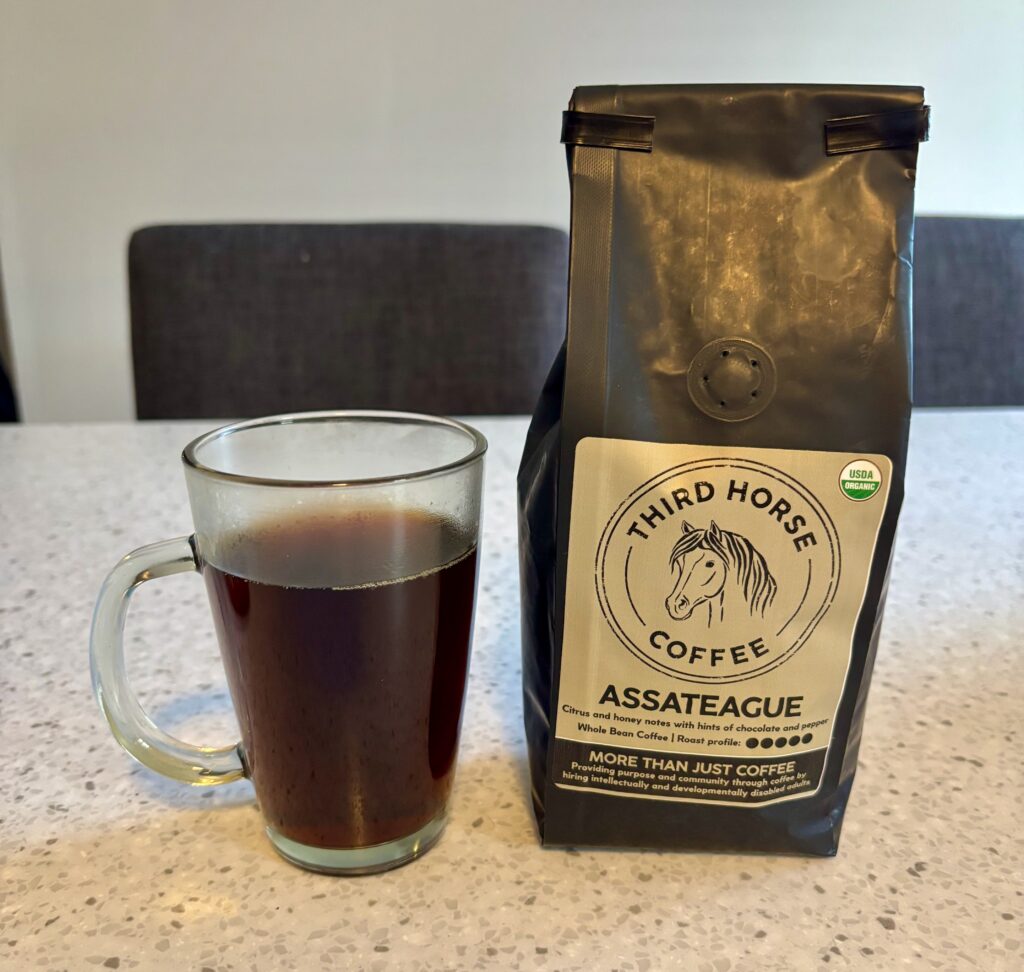 Third Horse Coffee Assateague whole bean coffee bag beside a mug of brewed coffee on a countertop.