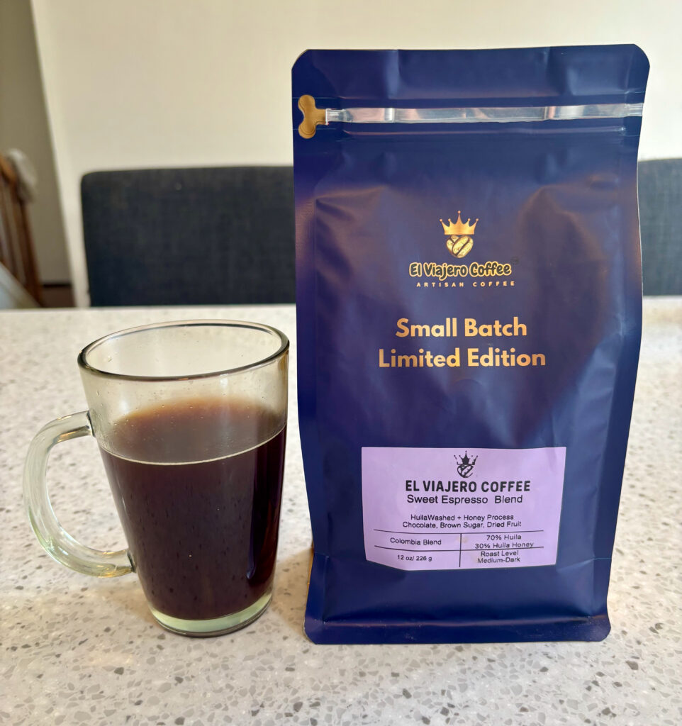 A glass mug filled with black coffee sits on a kitchen counter next to a blue bag of El Viajero Coffee Small Batch Limited Edition Sweet Espresso Blend.