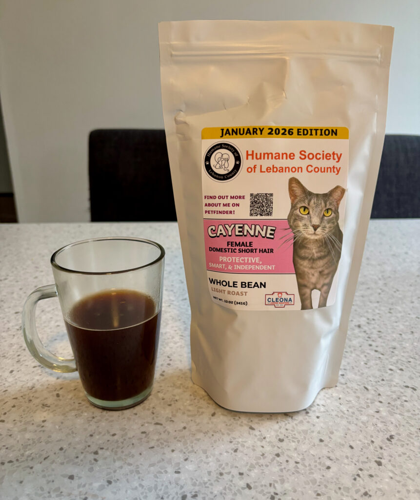 Cleona Coffee Roasters Humane Society Light Roast whole bean coffee bag featuring Cayenne the cat from Humane Society of Lebanon County, next to a glass cup of brewed coffee.