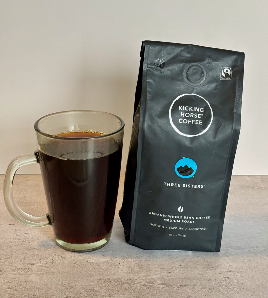 One of the Best Coffees to Try, a cup of Kicking Horse Three Sisters in a clear black mug next to the bag.