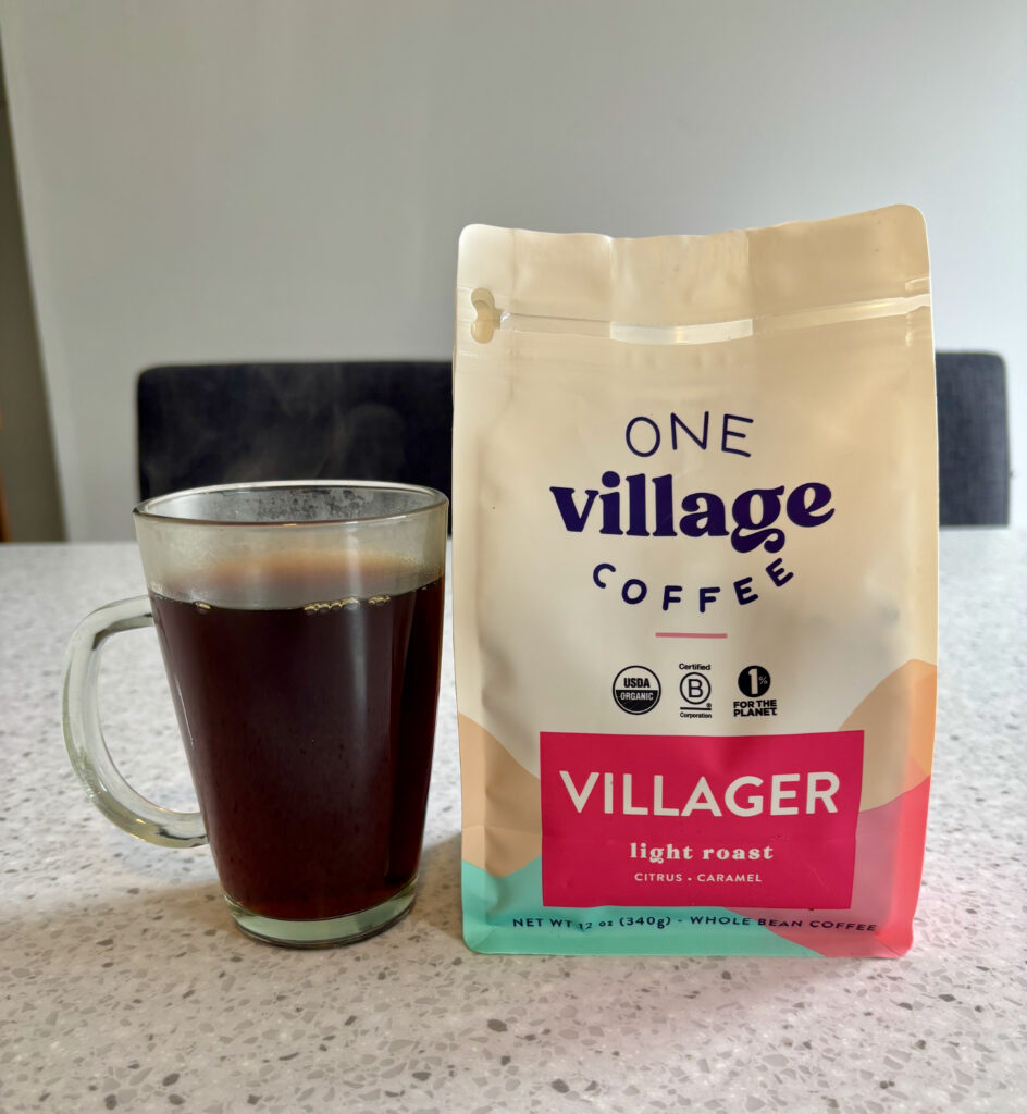 One of the Best Coffees to Try, a cup of One Village Villager in a clear black mug next to the bag.