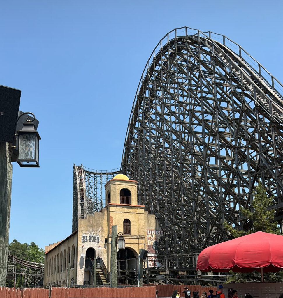Six Flags Great Adventure review photo of El Toro’s massive wooden structure and station building under a clear blue sky.