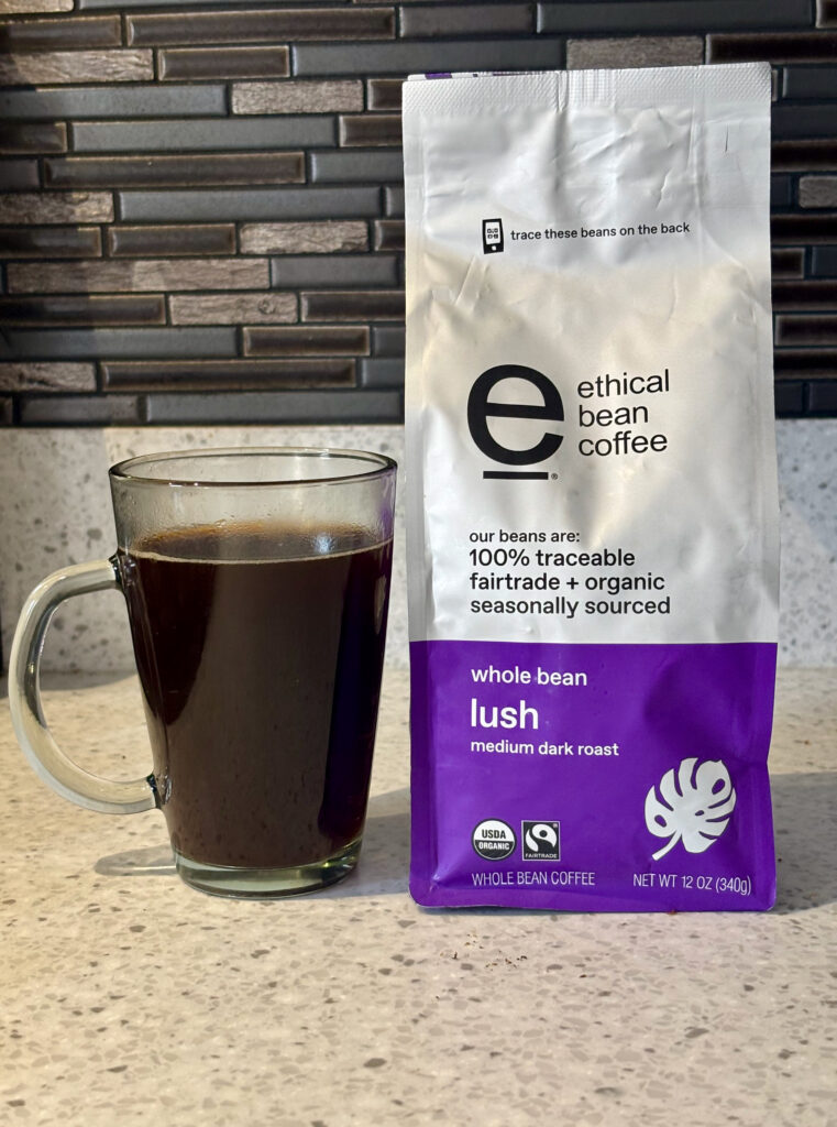 Ethical Bean Coffee Lush Review image showing black coffee in a glass mug next to an Ethical Bean Lush coffee bag on a minimalist counter.
