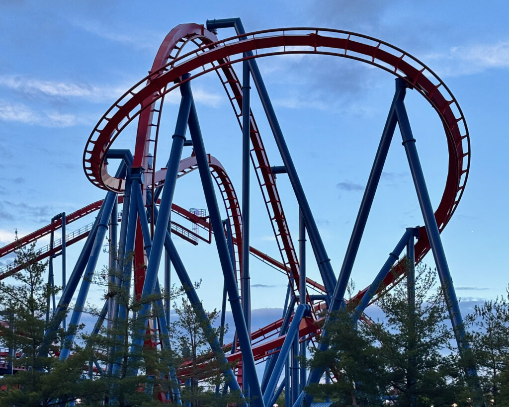 Six Flags Great Adventure review showing Superman: Ultimate Flight roller coaster and its signature pretzel loop at sunset.