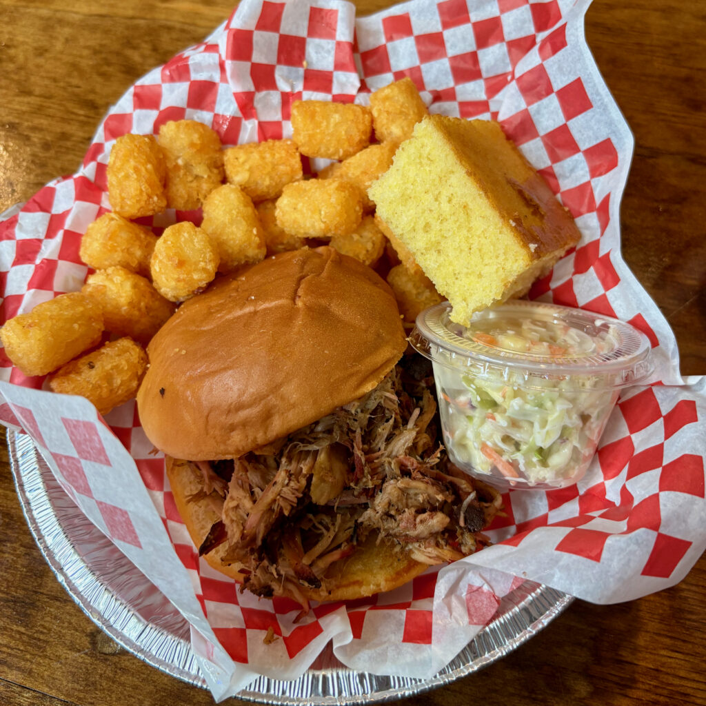 Six Flags Great Adventure review meal with a pulled pork sandwich, tater tots, cornbread, and coleslaw in a red checkered tray.