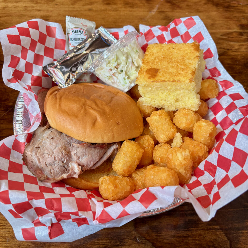 Six Flags Great Adventure review meal with a sirloin sandwich, tater tots, cornbread, coleslaw, and sauce packets in a red checkered food tray.