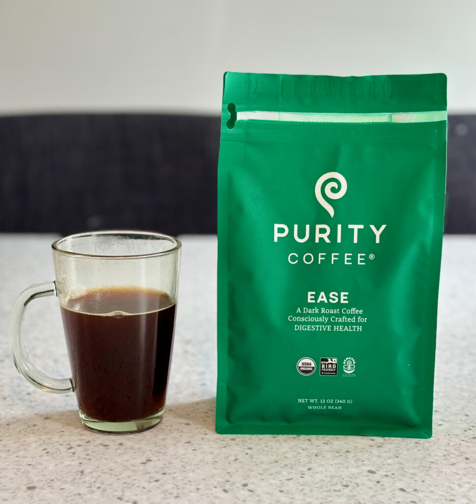 A green bag of Purity Ease used to show one of the best dark roast coffees, sitting next to a clear mug with black coffee