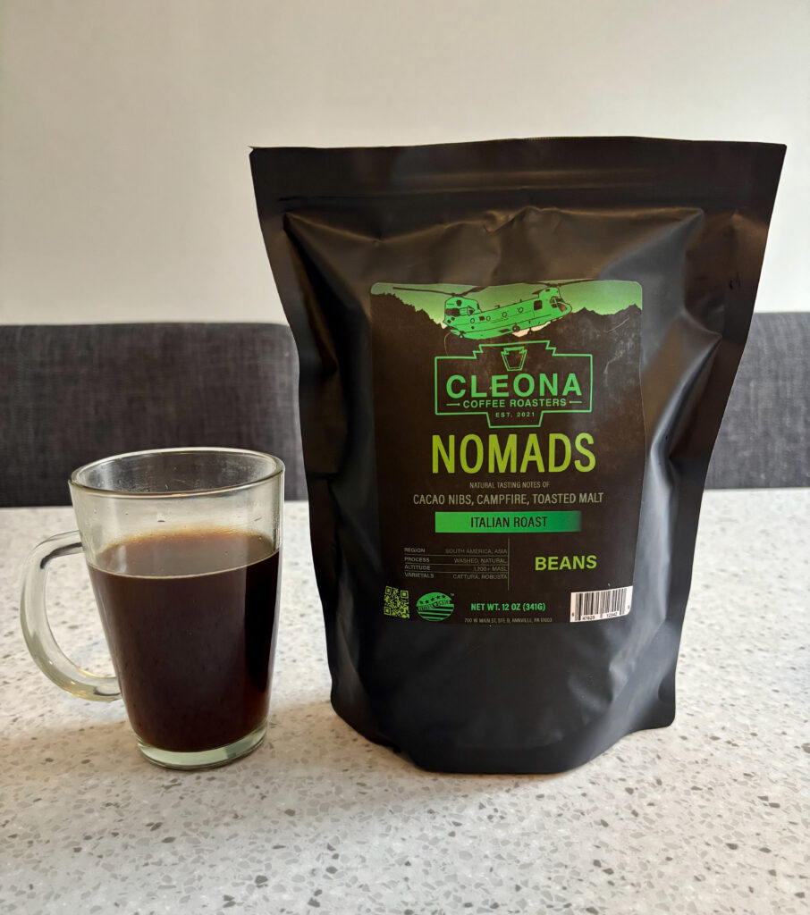 Cleona Coffee Roasters Nomads dark roast coffee bag with a clear glass mug of black coffee, one of the best dark roast coffees reviewed