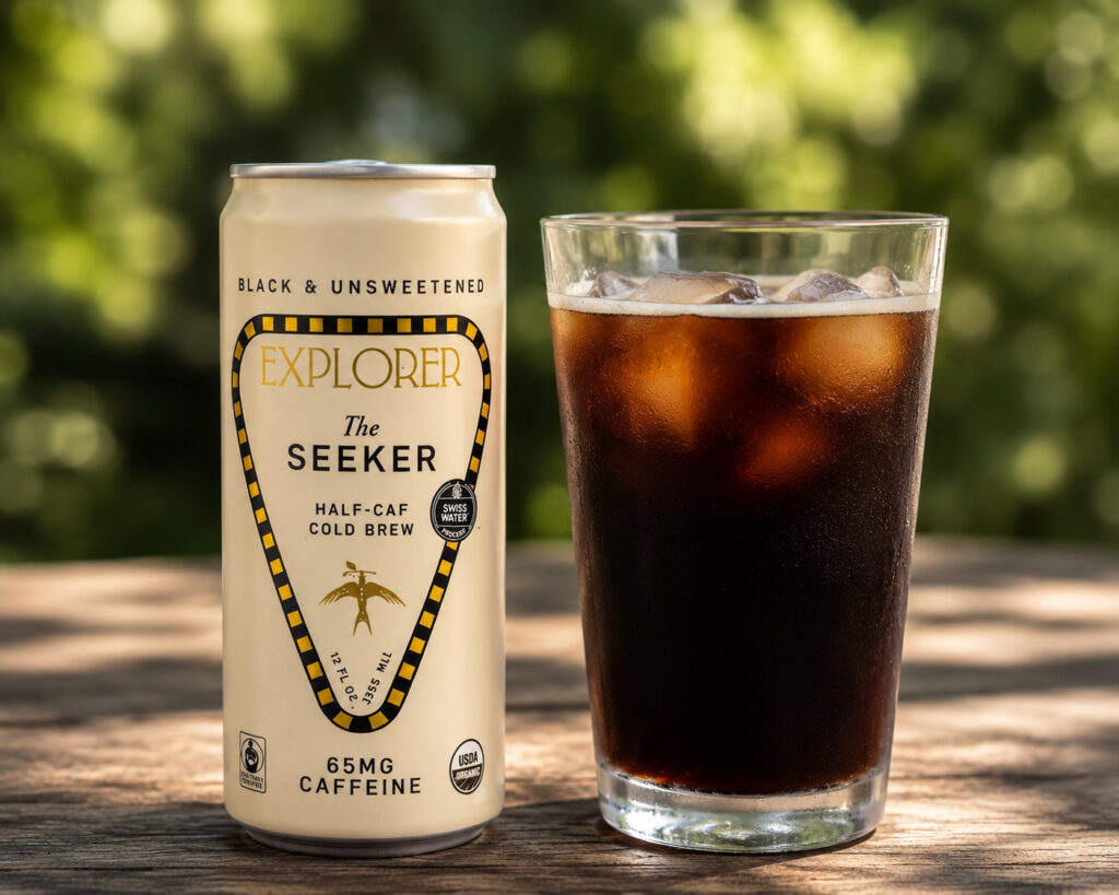 Explorer Coffee The Seeker Half-Caf Cold Brew Review image featuring a sleek can of Explorer Coffee The Seeker next to a glass of iced cold brew on a rustic wooden table, with a softly blurred green outdoor background emphasizing the drink as the focal point.