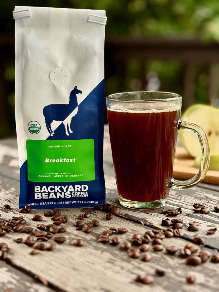 Backyard Beans Breakfast Blend Review: A bag of whole bean coffee next to a freshly brewed cup on a sunny wooden deck.