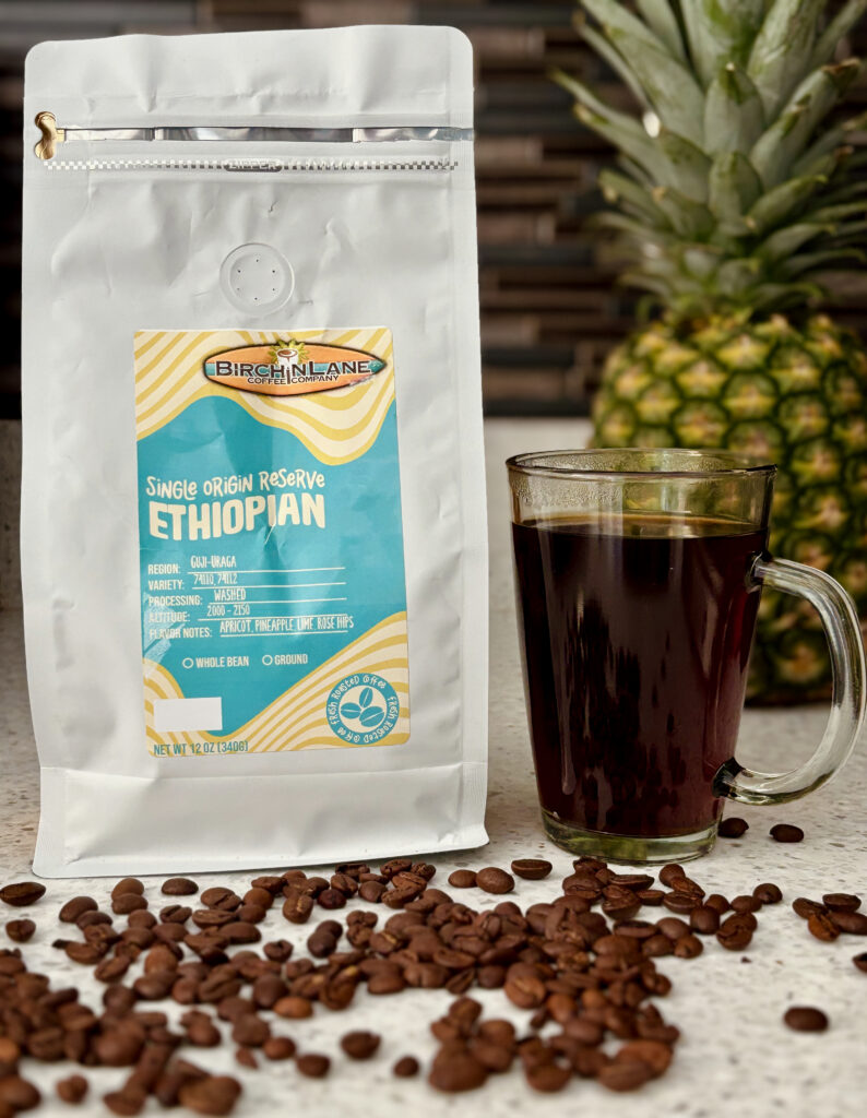 Birchin Lane Single Origin Ethiopian Coffee Review: One of My New Favorite Coffees featuring a bag of Birchin Lane Ethiopian beans, roasted coffee beans on a counter, a mug of pour-over coffee, and a pineapple background.